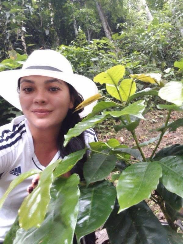 Mujer con sombrero junto a una planta de café